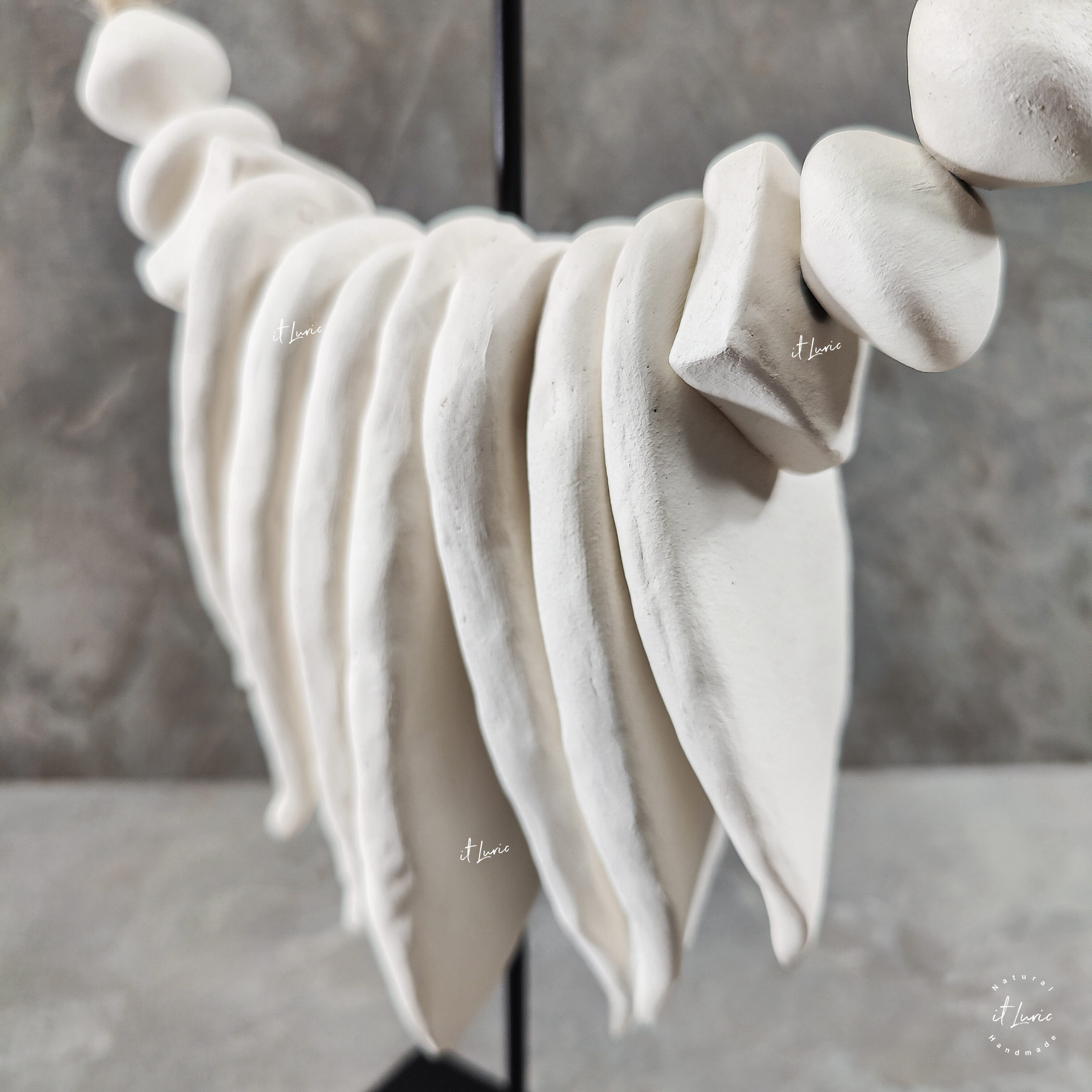 Colar em cerâmica branca, imitando folhas e algumas formas, acomodado em um pedestal em ferro preto